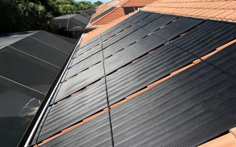 Solar pool heating collectors mounted on a terracotta tile roof, with the header pipe running along the top of the panels.